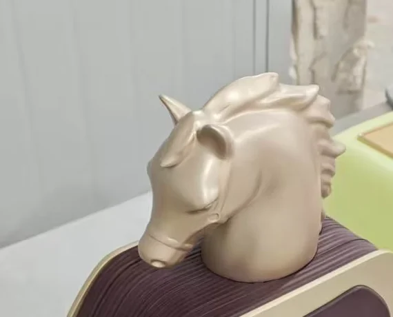 Satin gold horse head cap on a burgundy factice perfume bottle, photographed at three-quarter angle in the workshop