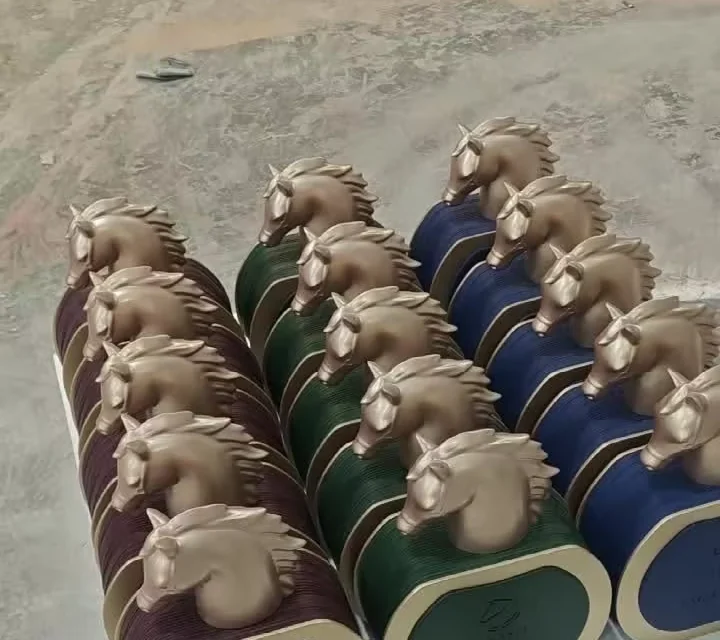 Nine factice perfume bottles in burgundy, green and blue laid out on a workshop floor, all with the same cast horse head cap
