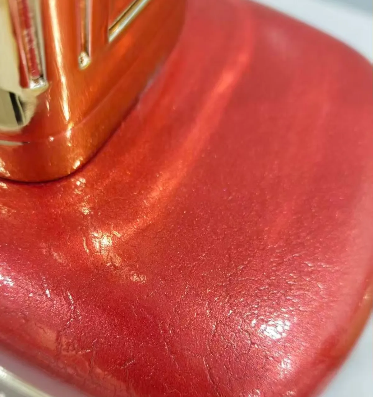 Close-up of a crackle lacquer surface in metallic red on the curved shoulder of a factice bottle, with the fine crack network clearly visible in raking light